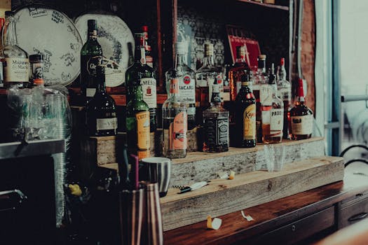 A collection of diverse liquor bottles including whisky, rum, and vodka displayed on a wooden bar shelf.