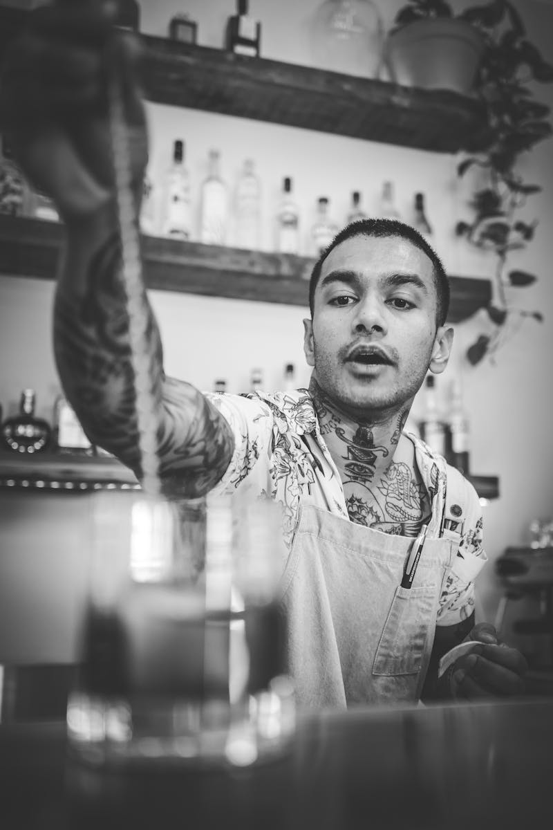 Tattooed bartender stirring a cocktail in a stylish bar. Black and white photo emphasizing artistic expression.