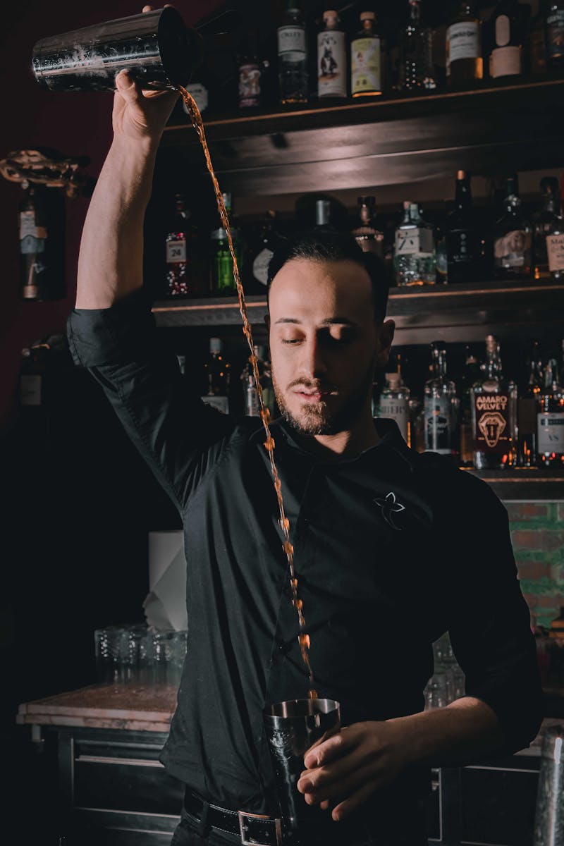 A skilled bartender precisely pouring a cocktail in a stylish bar with shelves of liquor.