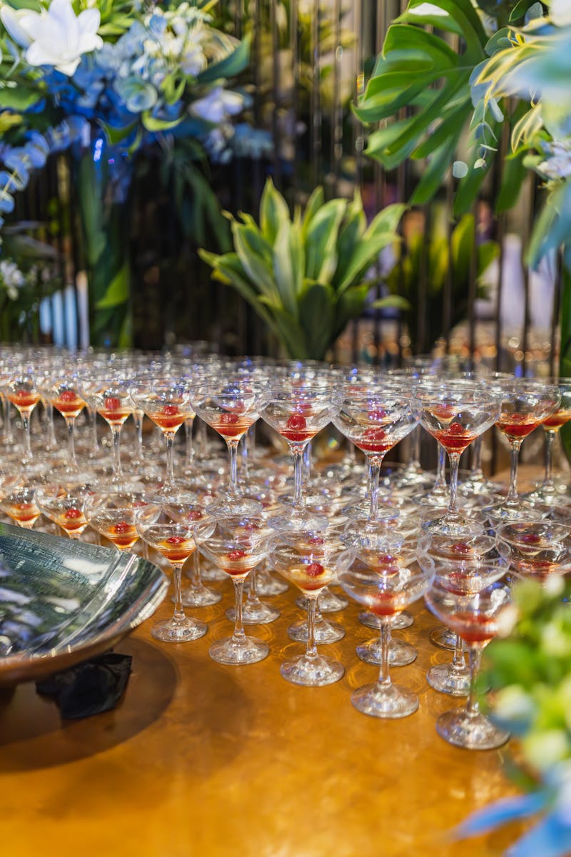 A stunning array of cocktail glasses filled with red liquid, surrounded by lush greenery and flowers, creating an elegant setting.
