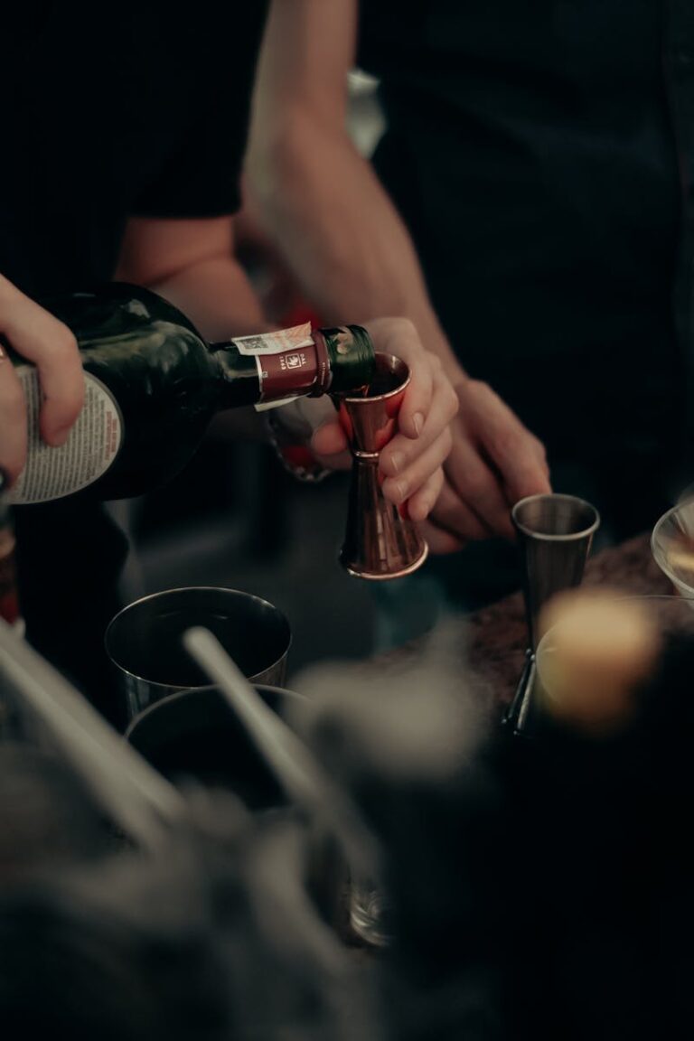 Closeup of bartender pouring drink in a busy, dimly lit bar environment.